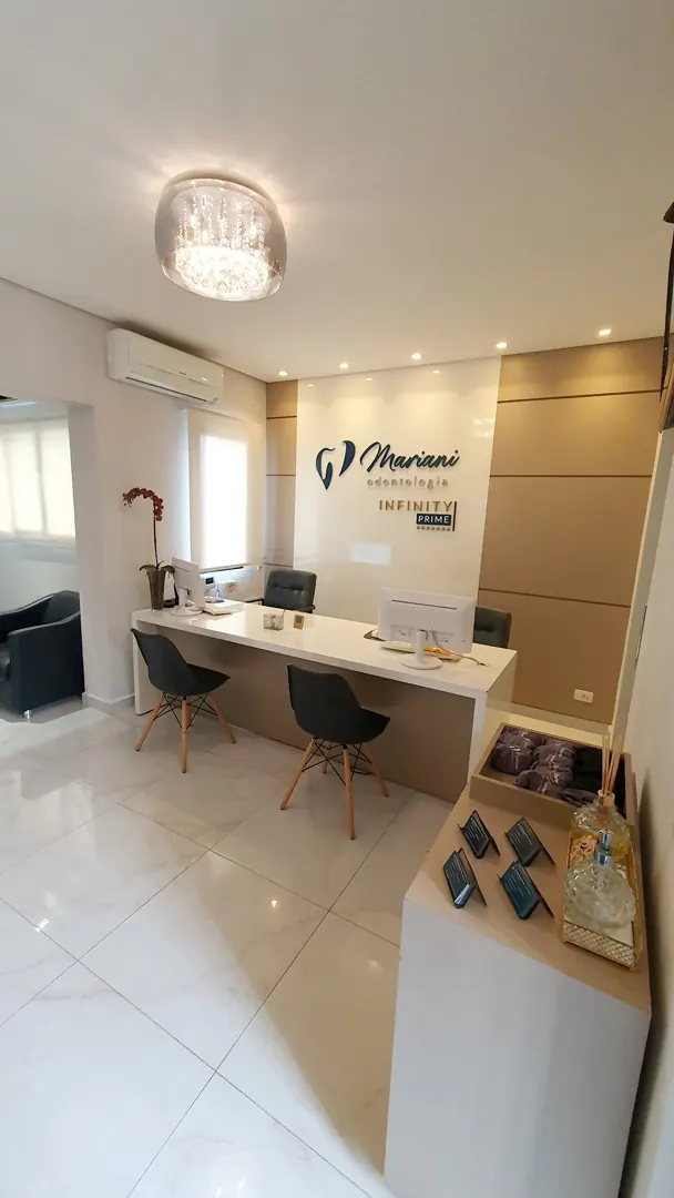 Recepção da clínica com bancada de atendimento e o logotipo da Mariani Odontologia na parede