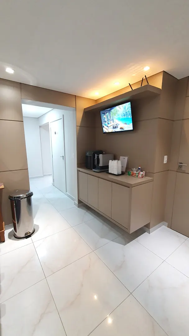 Corredor interno com bancada de apoio, televisão e piso porcelanato claro