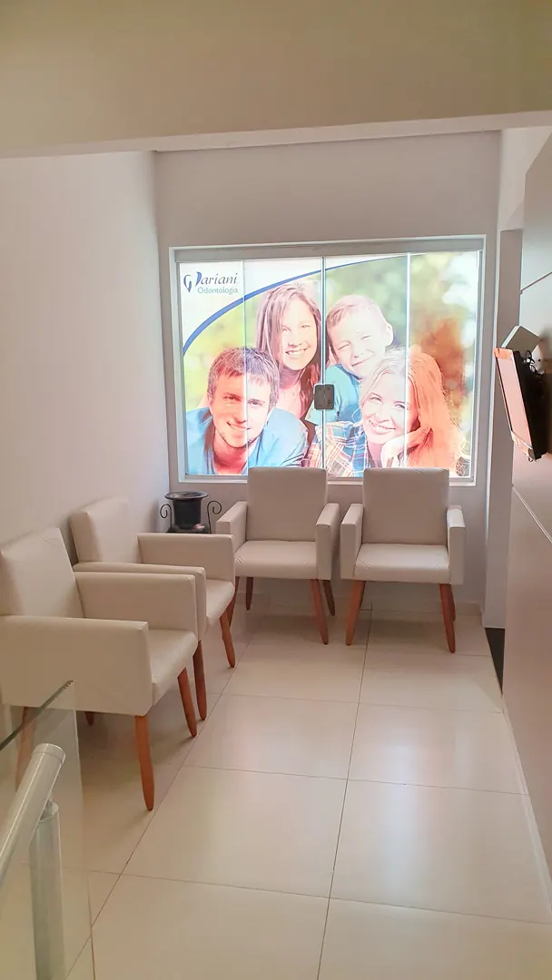 Sala de espera com poltronas e um painel iluminado de fotos de pacientes