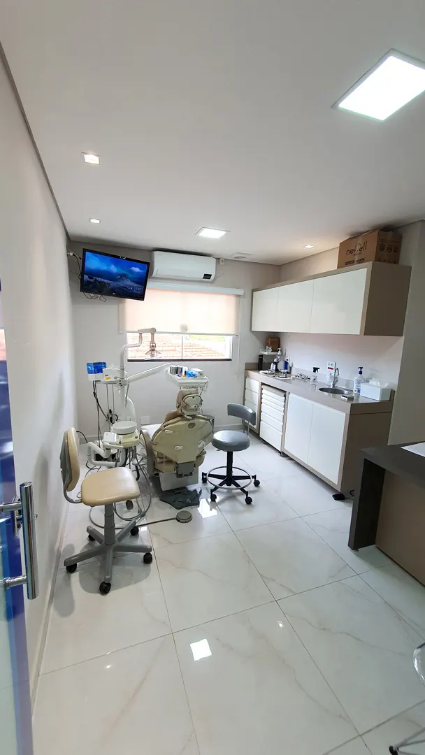 Consultório equipado com cadeira odontológica, televisão e armários de apoio