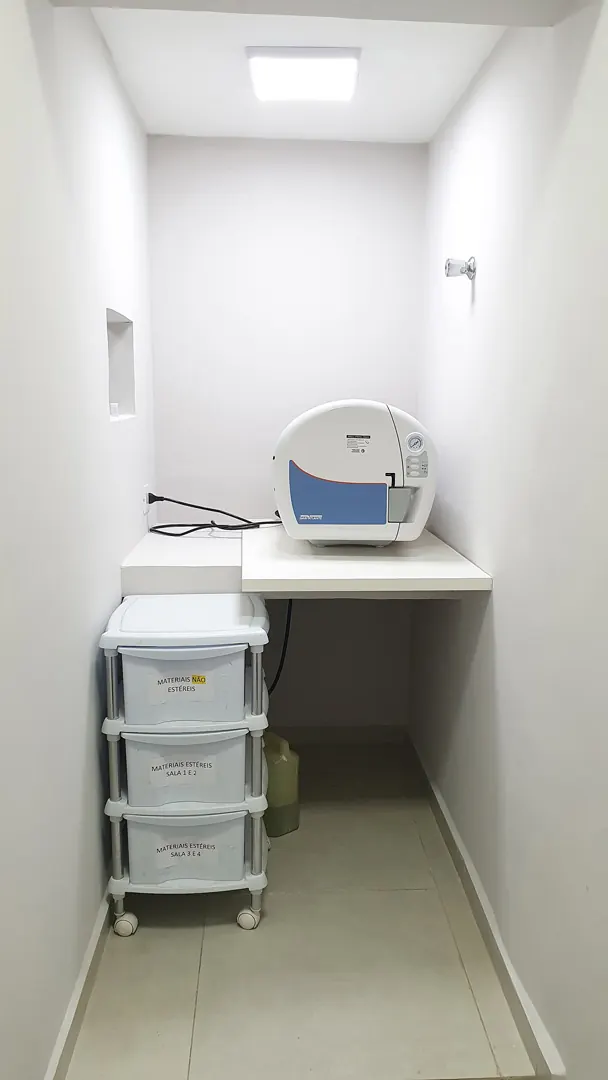 Sala de esterilização com autoclave sobre a bancada e carrinho de instrumentos