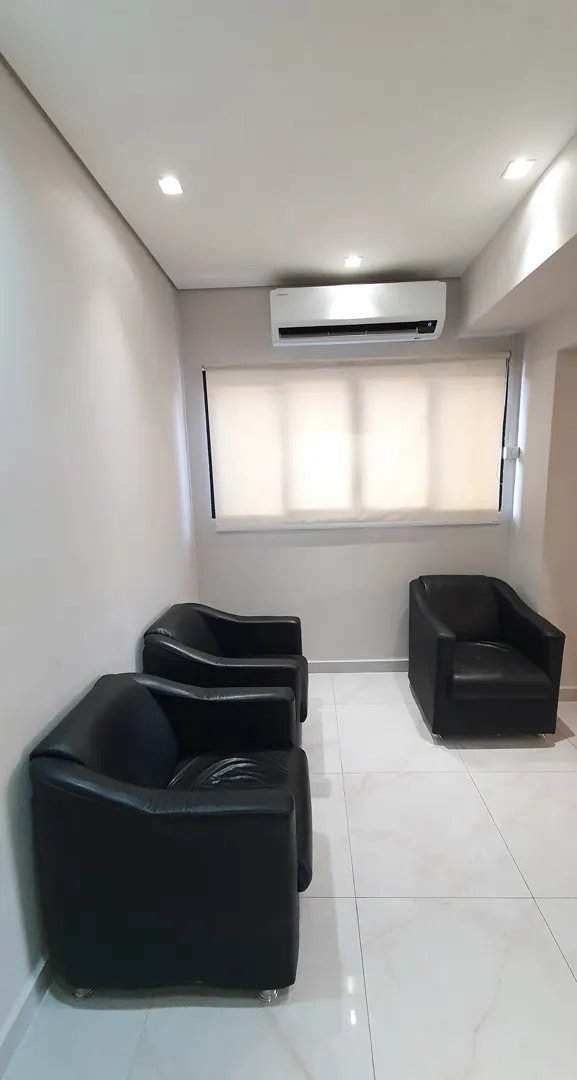 Sala de espera com poltronas pretas e janela com persiana
