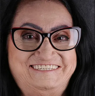 Retrato de uma paciente de óculos sorrindo após o tratamento, em estúdio sobre fundo escuro