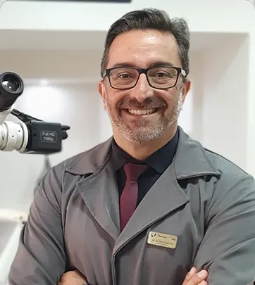 Dr. Rodrigo Mariani de braços cruzados, de jaleco da clínica, ao lado do microscópio operatório