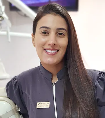 Dra. Jacqueline Cristina sorrindo, de jaleco da clínica, dentro do consultório