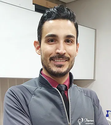 Dr. Thiago Mariani sorrindo, de jaleco da Mariani Odontologia, em uma sala de atendimento